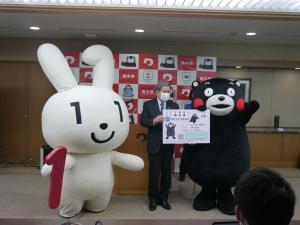 マイナちゃんの立ち合いのもと、くまモンにマイナンバーカードを交付する蒲島知事の写真