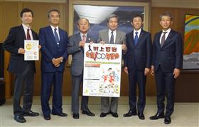 実行委員会のメンバーと記念事業のポスターを持つ蒲島知事